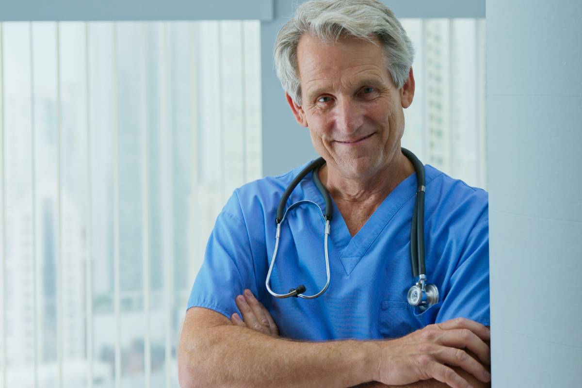 An older nurse poses for a photo while discussing the average age of retirement of nurses.