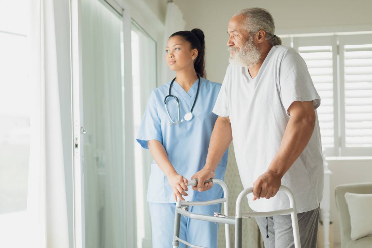 A healthcare professional assists a patient at home while discussing their home health aide salary expectations.