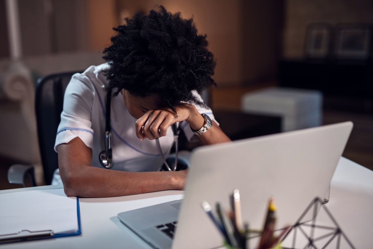 A physician, subject to the third of several healthcare layoffs, puts her head down in anguish.
