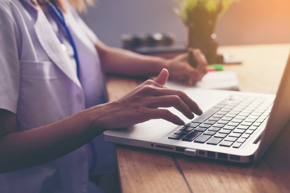 A nurse uses a laptop to write their nurse manager cover letter.