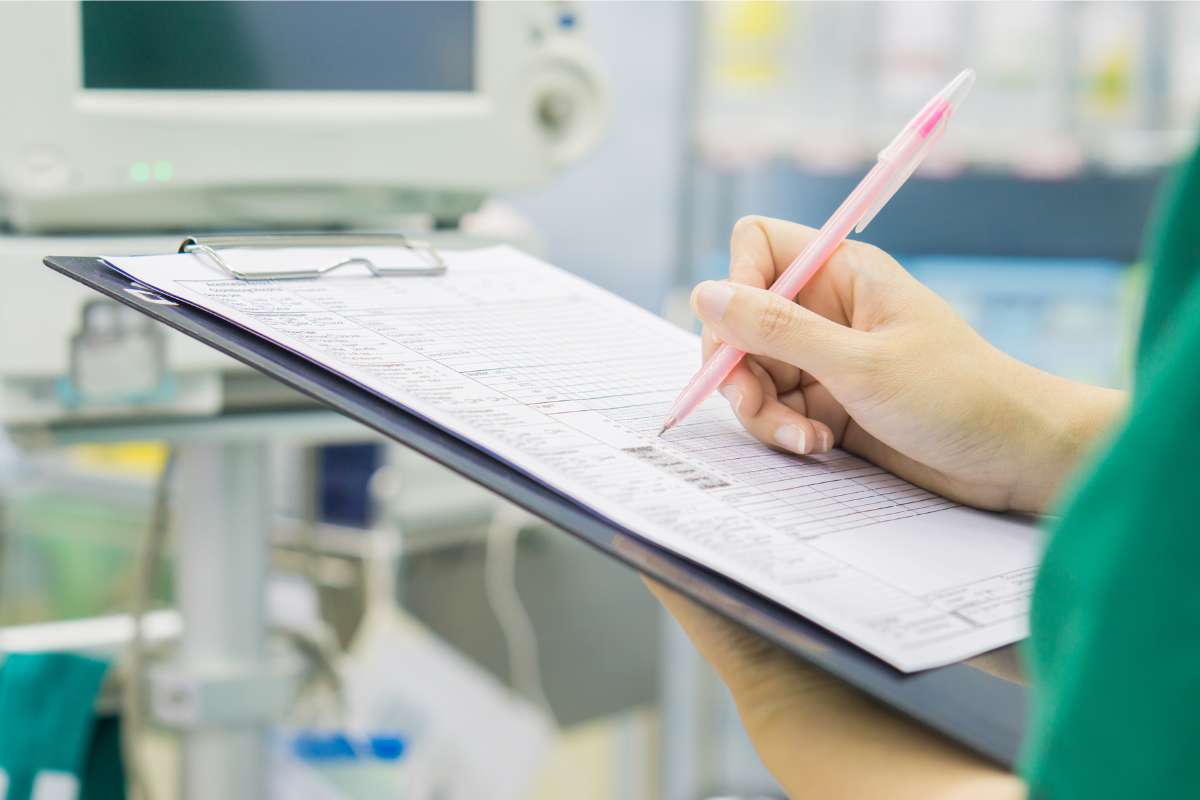 A clipboard with papers on it and a nurse writing on it.