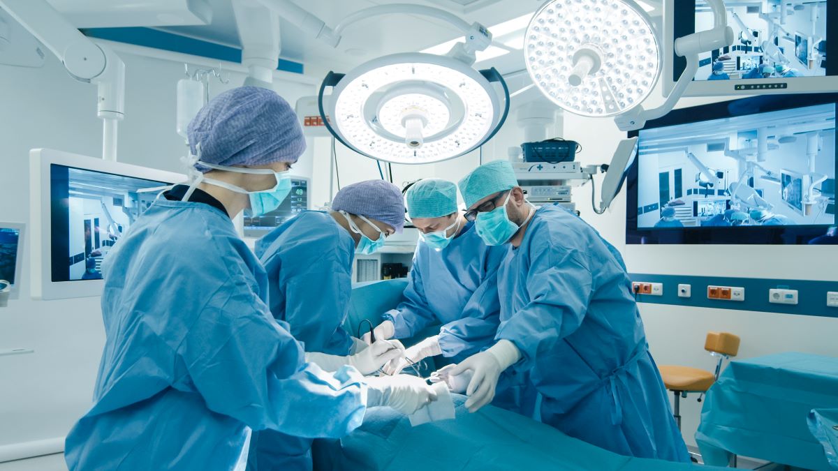 A surgeon, OR nurse, and other surgery staff work on a patient.