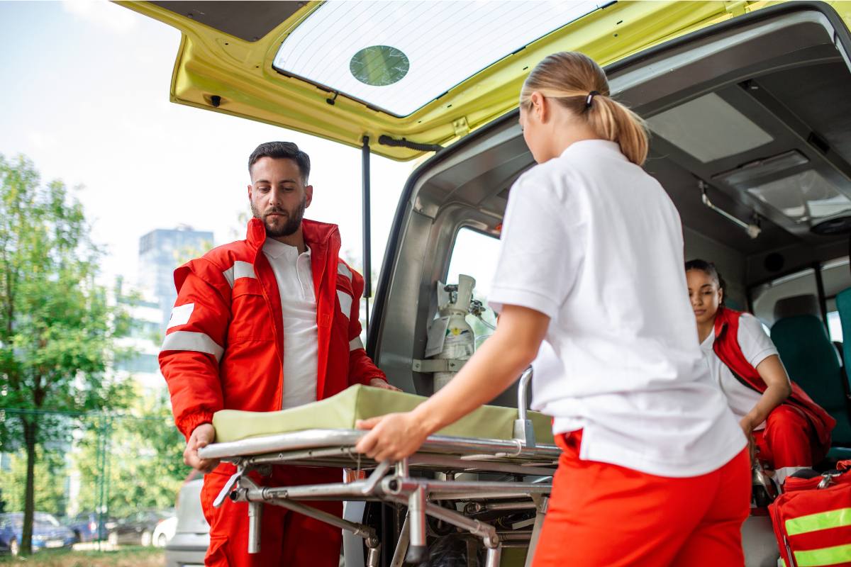 Two first responders load a stretcher into a van while discussing paramedic-to-RN bridge programs.