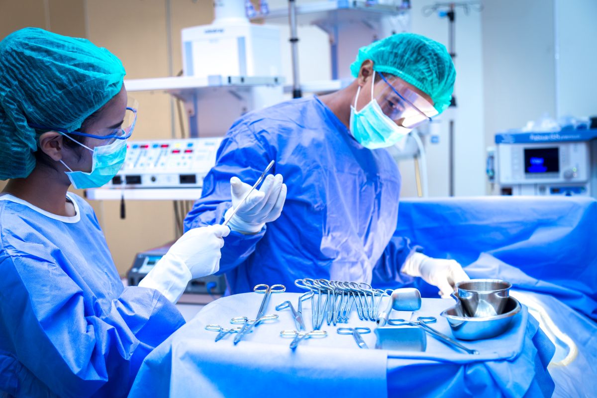 A surgical tech hands the supervising surgeon a tool.